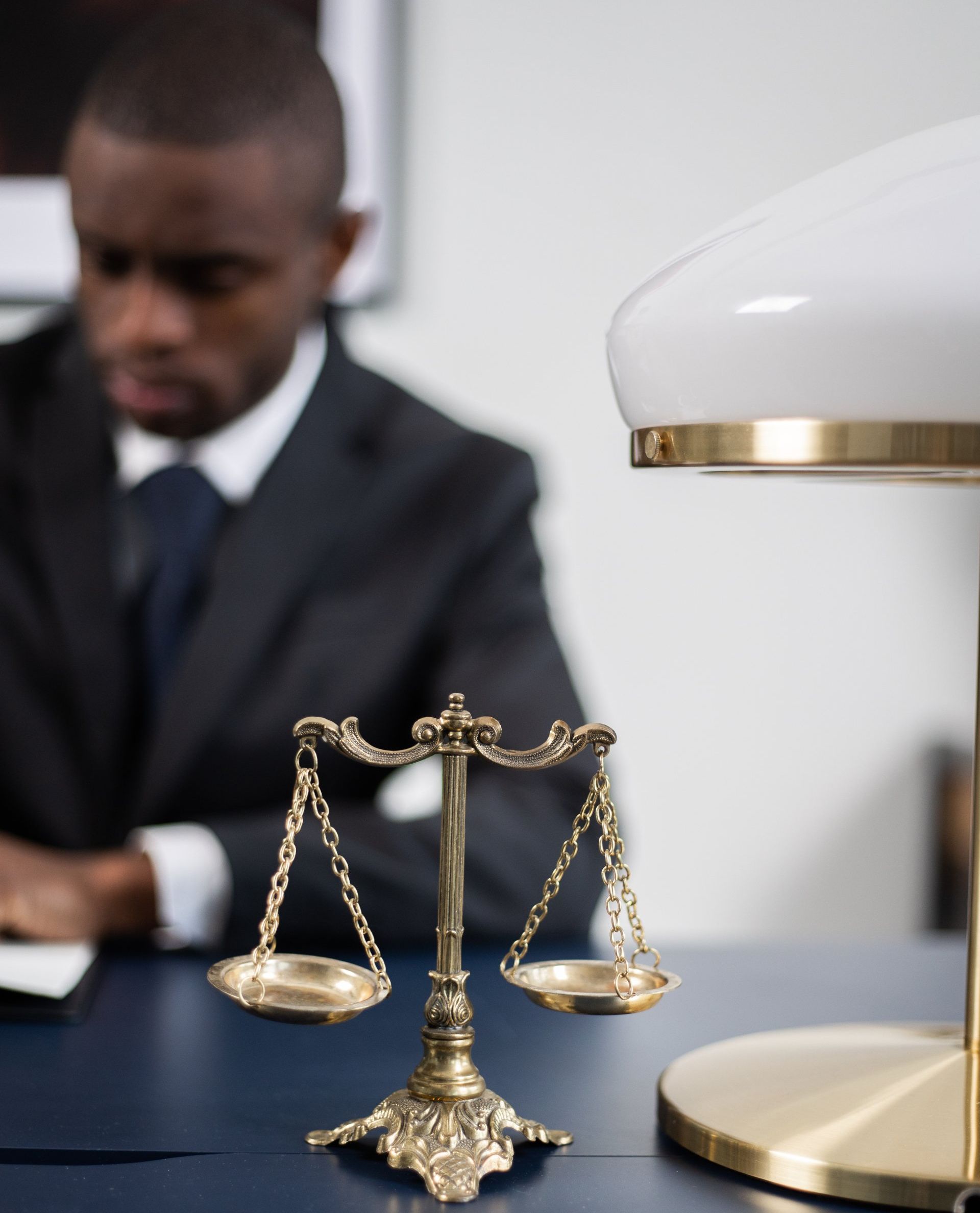 a man in a suit sits at a desk next to a scale of justice