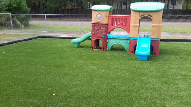 Play structure with green and brown elements on a green artificial lawn.