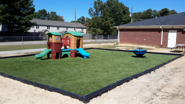 Playground with green turf, play structure, and spinning seat, bordered by black and beige.