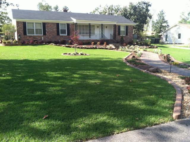 Well-maintained ranch-style house with manicured lawn, brick walkway, and landscaping.