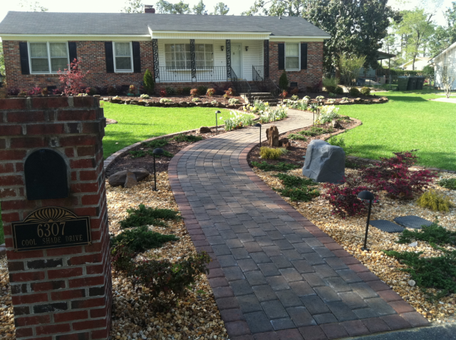 Brick pathway leading to a brick house with a well-manicured lawn and landscaping.