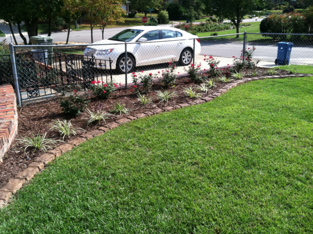 White car parked in driveway, landscaped yard with curb edging and green lawn.