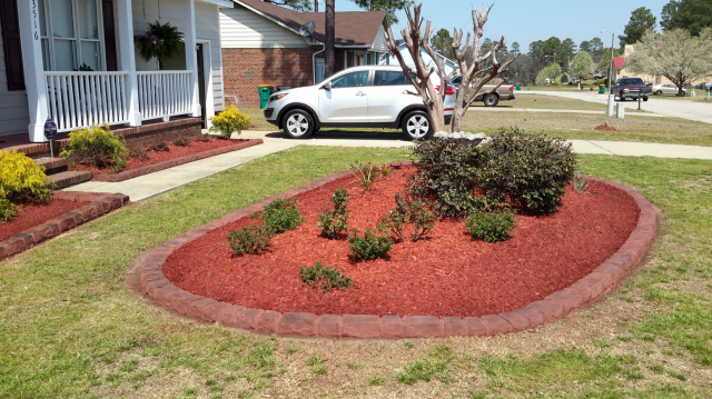 Landscaped front yard with red mulch borders, white SUV, and home.