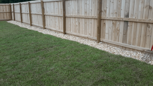 Wooden fence with gravel border next to green grass.