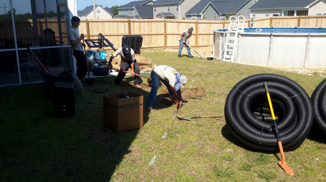 Construction workers installing drainage pipes in a backyard near a pool.