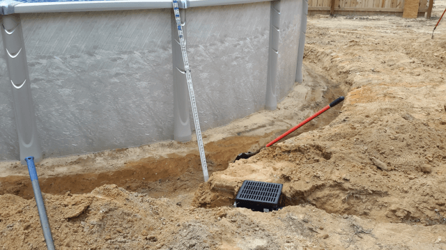 Construction site with an above-ground pool, dirt, and drainage grate.