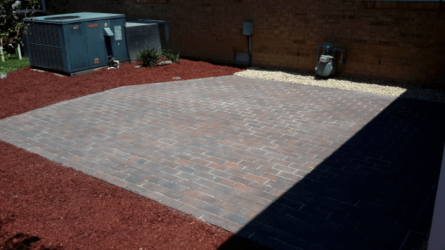 Brick patio surrounded by red mulch. Two AC units sit nearby.