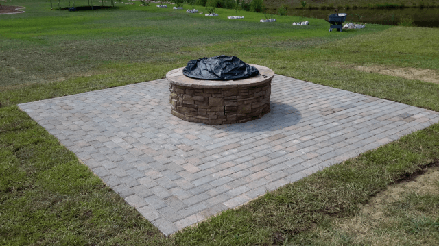 Fire pit on stone patio in grassy yard.