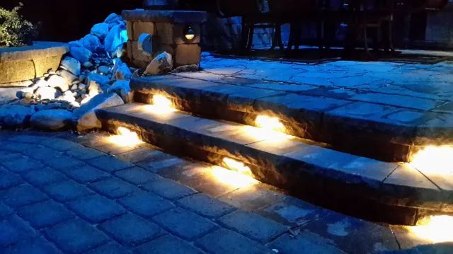 Stone steps with built-in lights leading up, illuminated at night. Blue-toned paving surrounds.