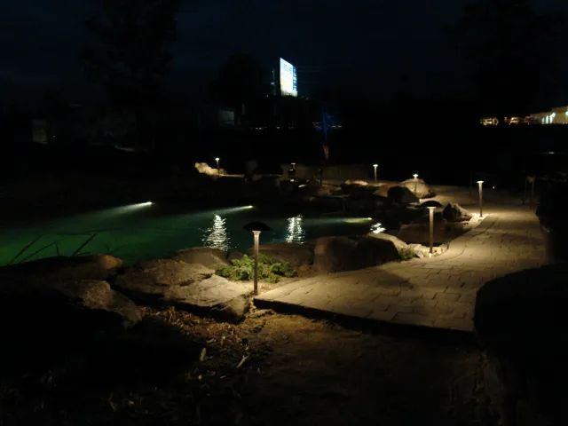 Night view of a lit outdoor pond with path and fountain lights.