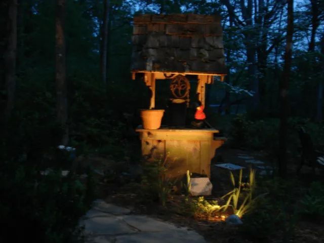 A well illuminated at night in a wooded area, stone construction with a bucket and rope.