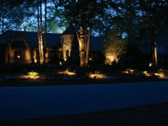 House at night with landscape lighting illuminating trees and facade.