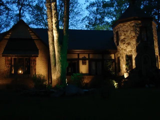 Stone house illuminated at night with a tower, trees, and dark blue sky.