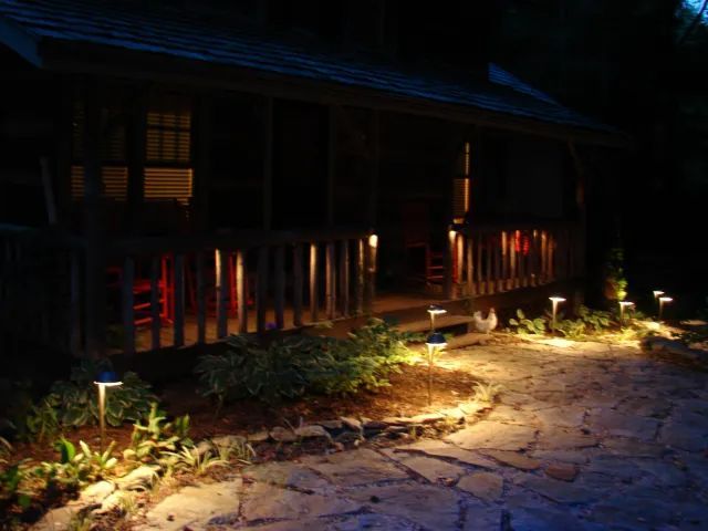 Pathway and porch illuminated with landscape lighting at night.