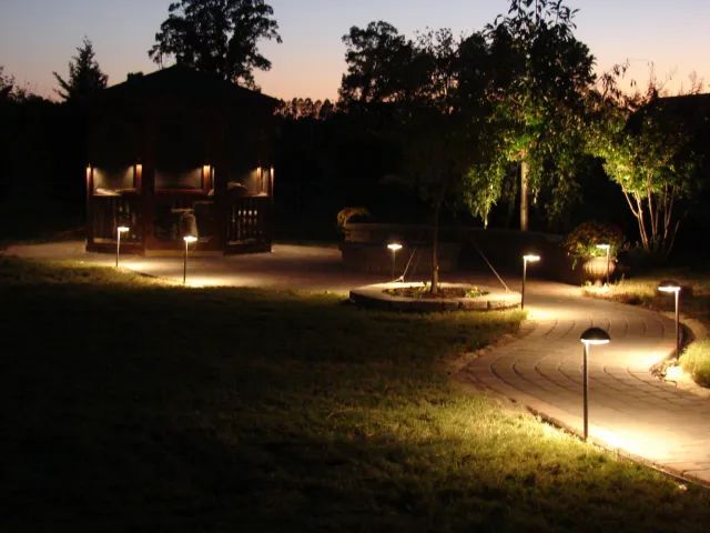 Pathway and gazebo illuminated by outdoor lights at dusk.