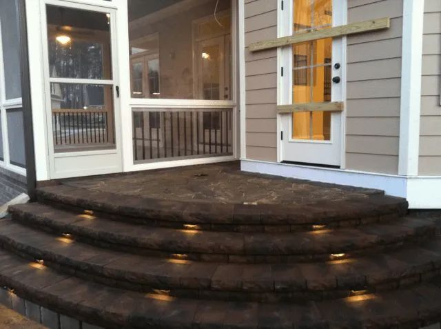 Stone steps with built-in lights lead to a house entrance with a screen door and a wooden door.