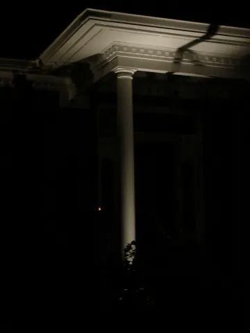 A white column supporting a building's ornate ceiling in the dark.