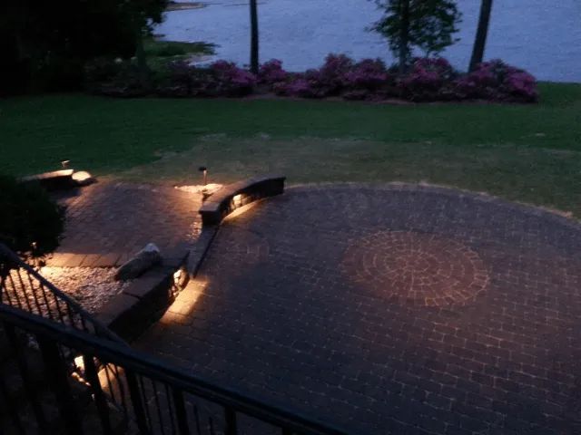 Brick patio with low lighting at dusk, overlooking a body of water and flowers.