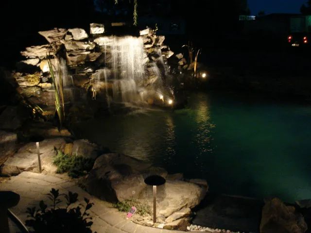 Waterfall illuminated at night with lights reflecting in the pond.