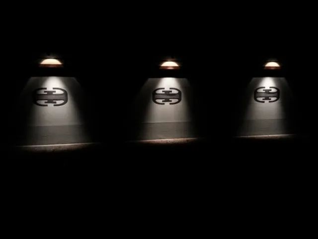 Three spotlights shining on the Gucci logo in a dark setting.