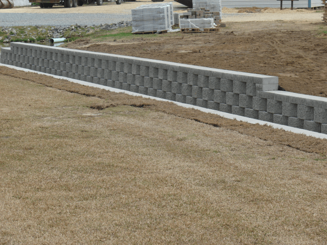 Gray retaining wall made of interlocking blocks on brown grass.