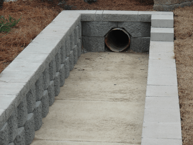 Concrete drainage channel with a pipe outlet in a grassy area.