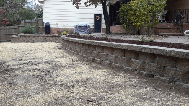 Retaining walls surrounding a dirt yard, leading to a house with a dark blue door.