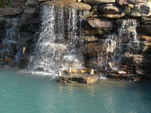 Waterfall cascading into a turquoise pool, built of layered brown rocks.