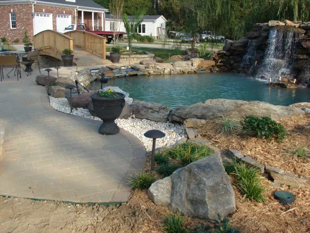 Scenic backyard with pond and waterfall; stone and concrete landscaping.