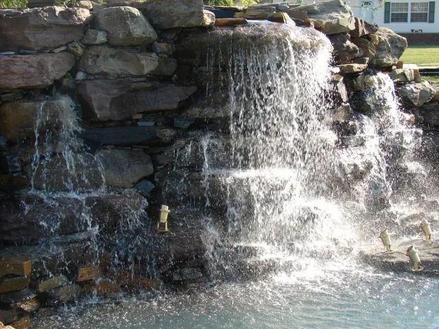Waterfall cascading over rocky structure into a pool. Water is spraying and reflecting sunlight.