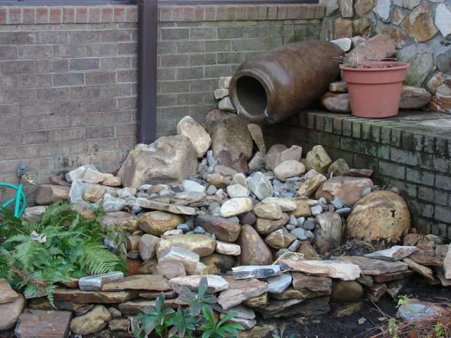 Stone water fountain with a large, tilted pot and surrounding rocks.