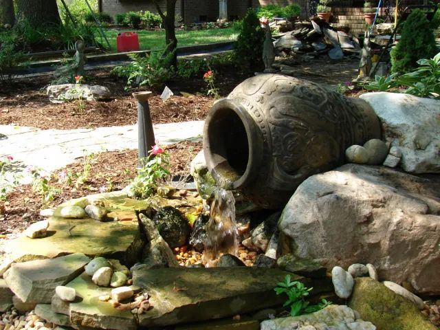 Water flows from a large decorative urn into a rock-lined garden feature.