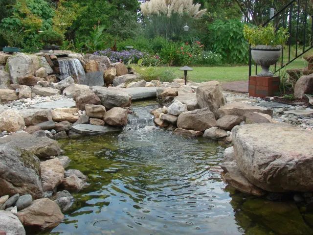Water feature with a waterfall and pond surrounded by rocks and greenery.