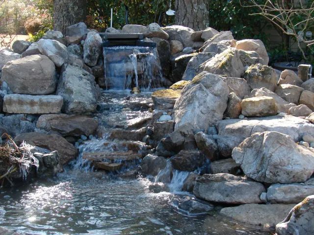 Water cascades down a rocky waterfall into a small pond, sunlight glinting on the surface.