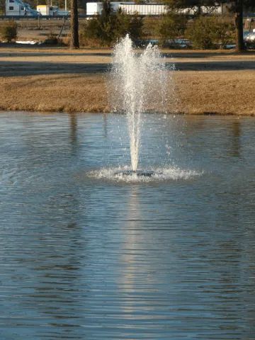 Fountain spraying water high into the air in a pond; water ripples.