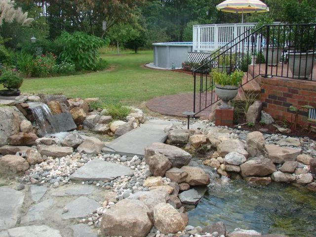 Backyard landscape with waterfall, stone path, pool, and deck.