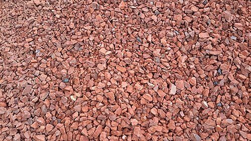 Red gravel, close-up view; small, reddish-brown stones cover the ground.