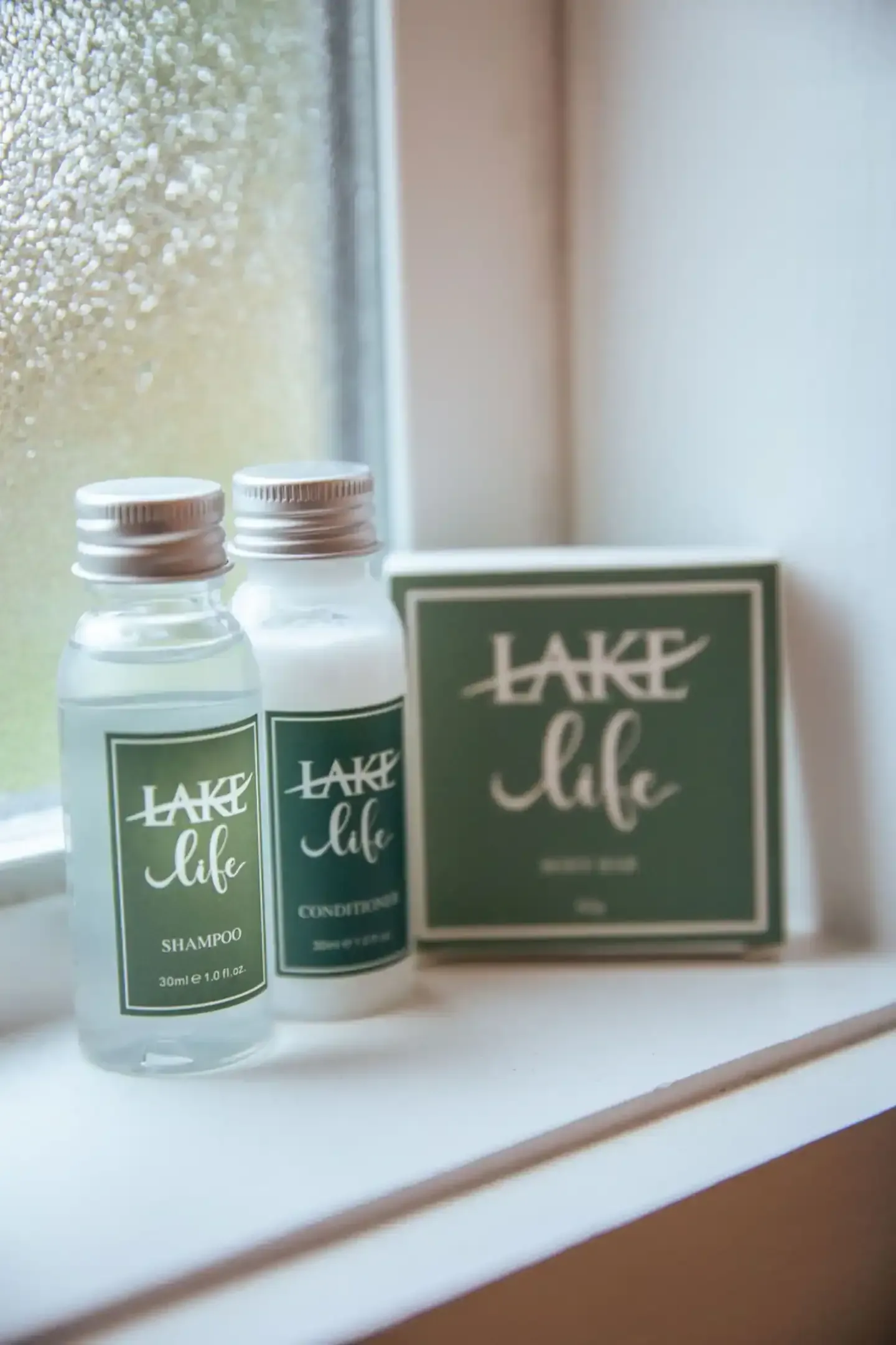 Two bottles of lotion and a box of soap are sitting on a window sill.