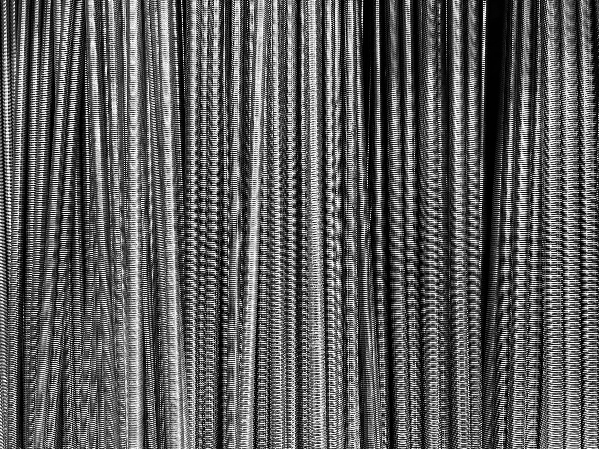 Primo piano di numerose barre di acciaio verticali disposte vicine tra loro, creando una superficie strutturata in tonalità di grigio.