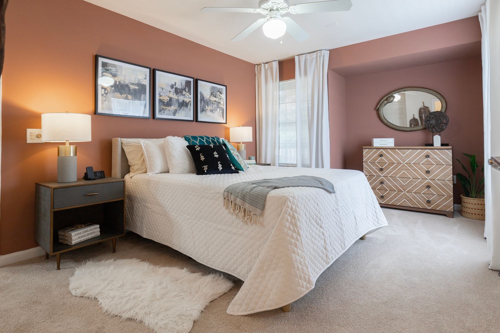 A bedroom with a bed , dresser , nightstand , mirror and ceiling fan.