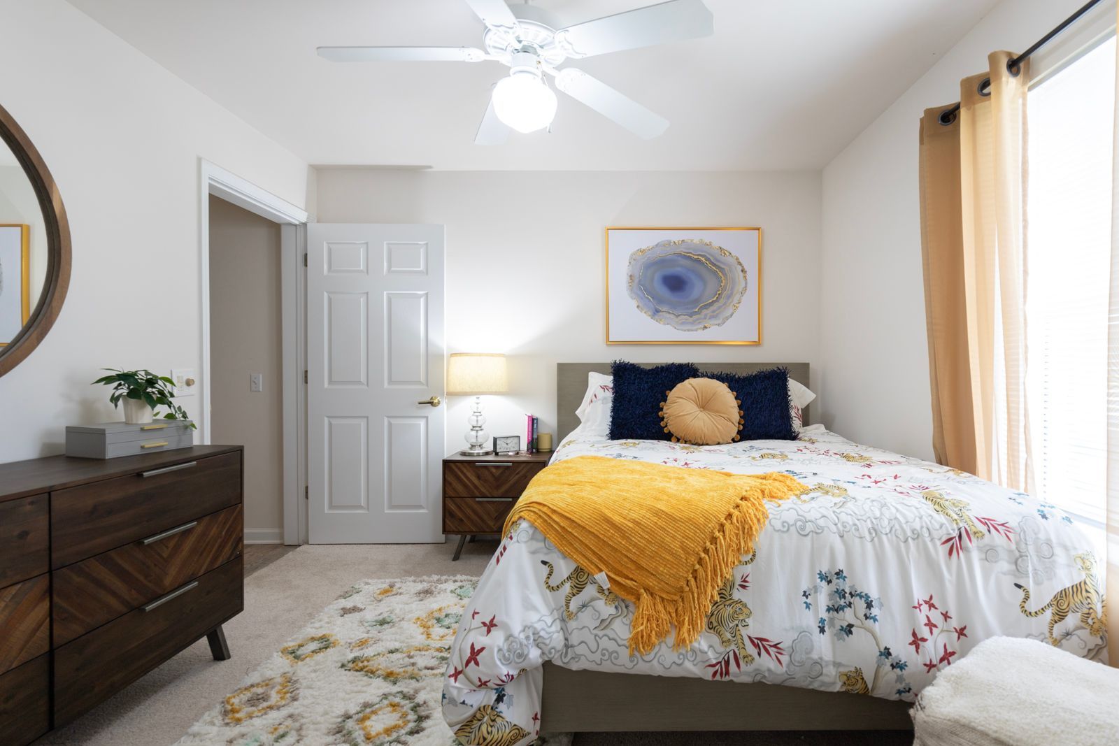 A bedroom with a bed , dresser , mirror and ceiling fan.