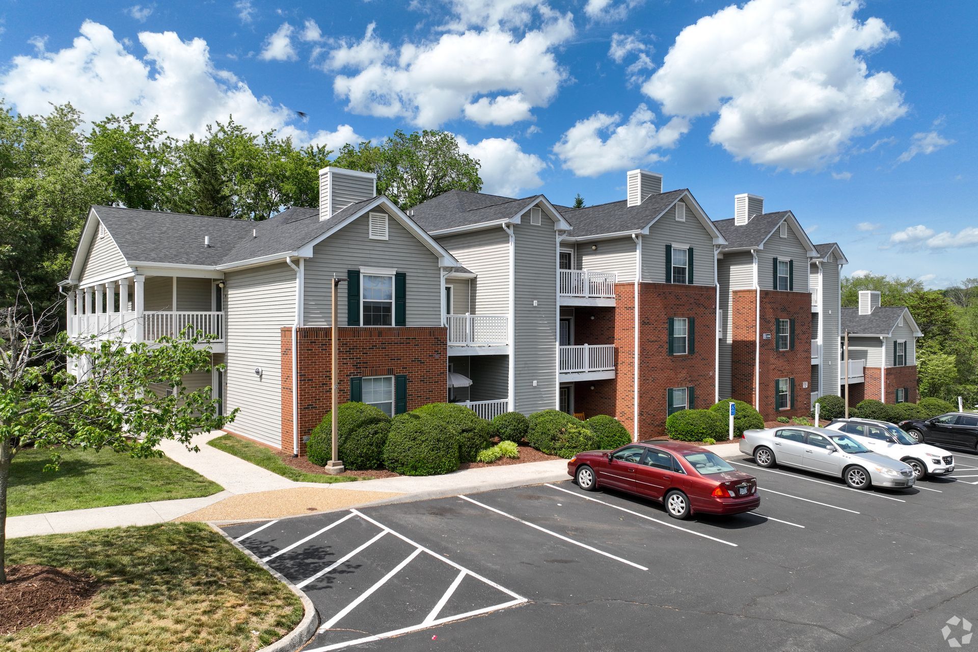Apartment building with brick accents, parked cars, and a sunny, blue sky.