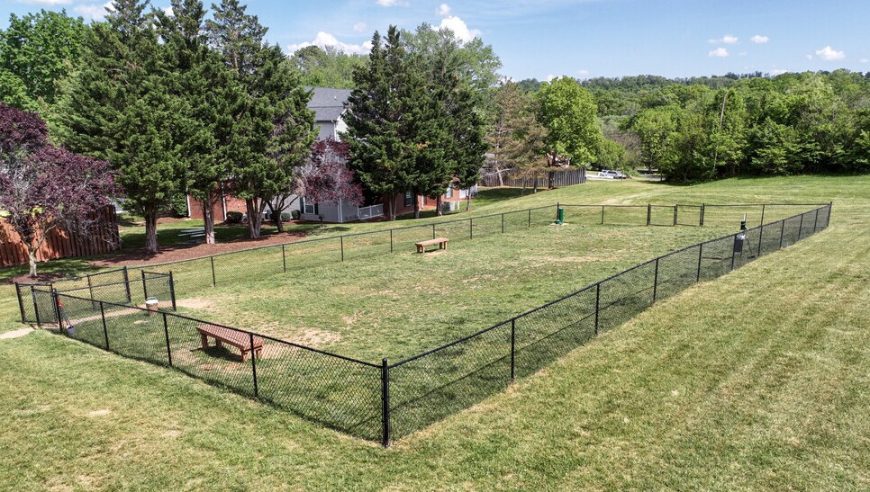 Black fenced dog park with bench and grass. House and trees in background.