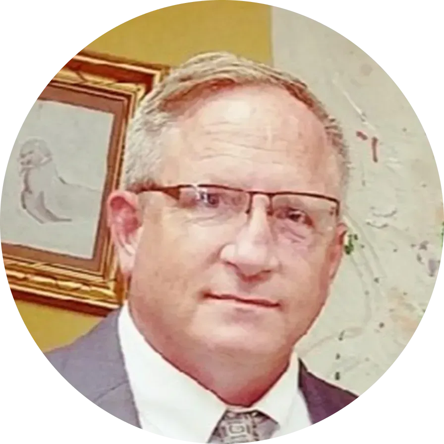 Man with glasses, wearing a suit, smiling slightly, in front of a painting.