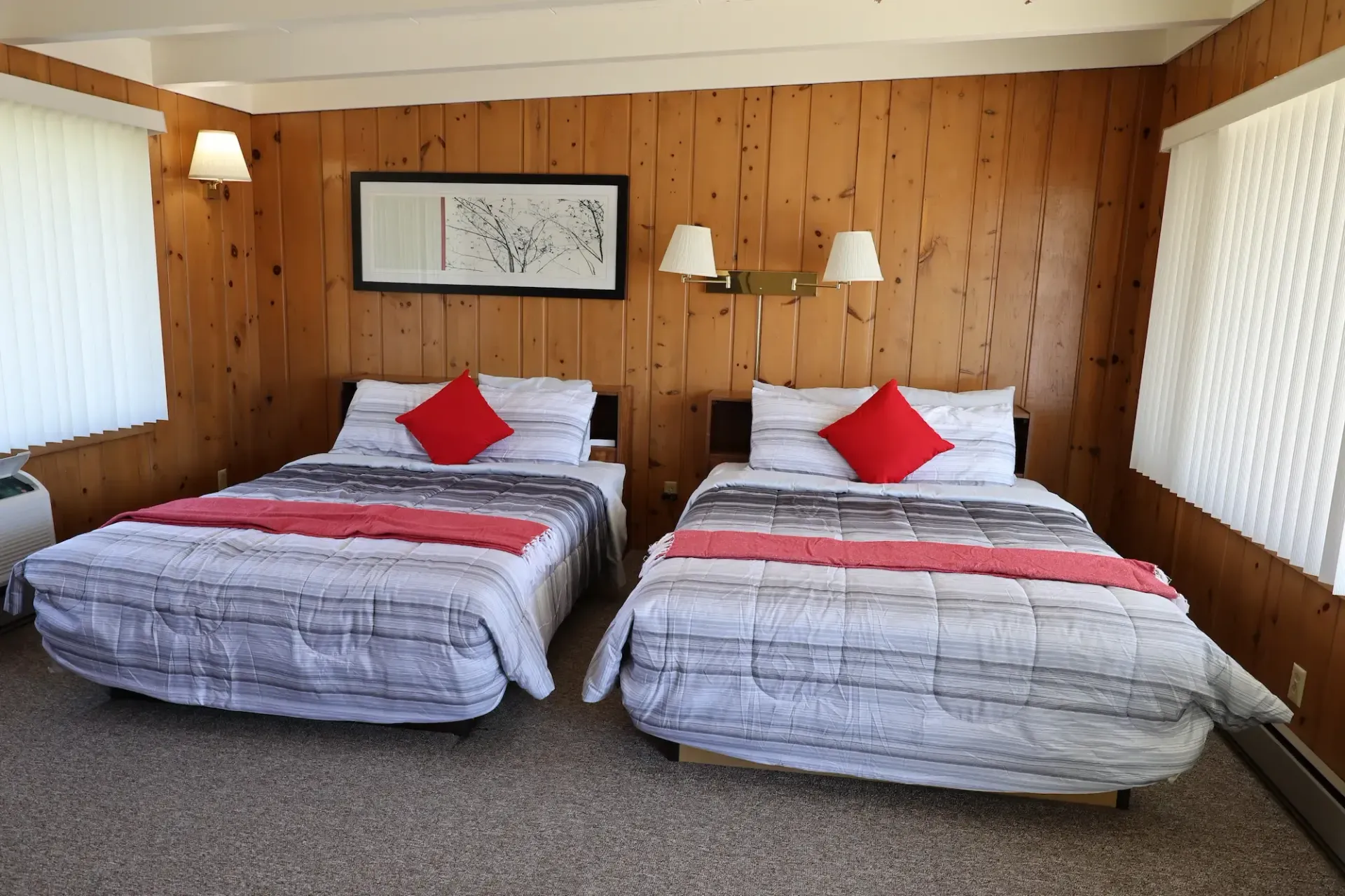 There are two beds in the room with wood paneling.