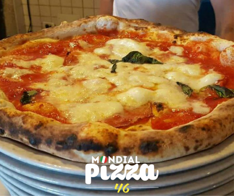 Una pizza Margherita appena sfornata con mozzarella fusa, salsa di pomodoro e basilico su una pila di piatti da Mondial Pizza 46.