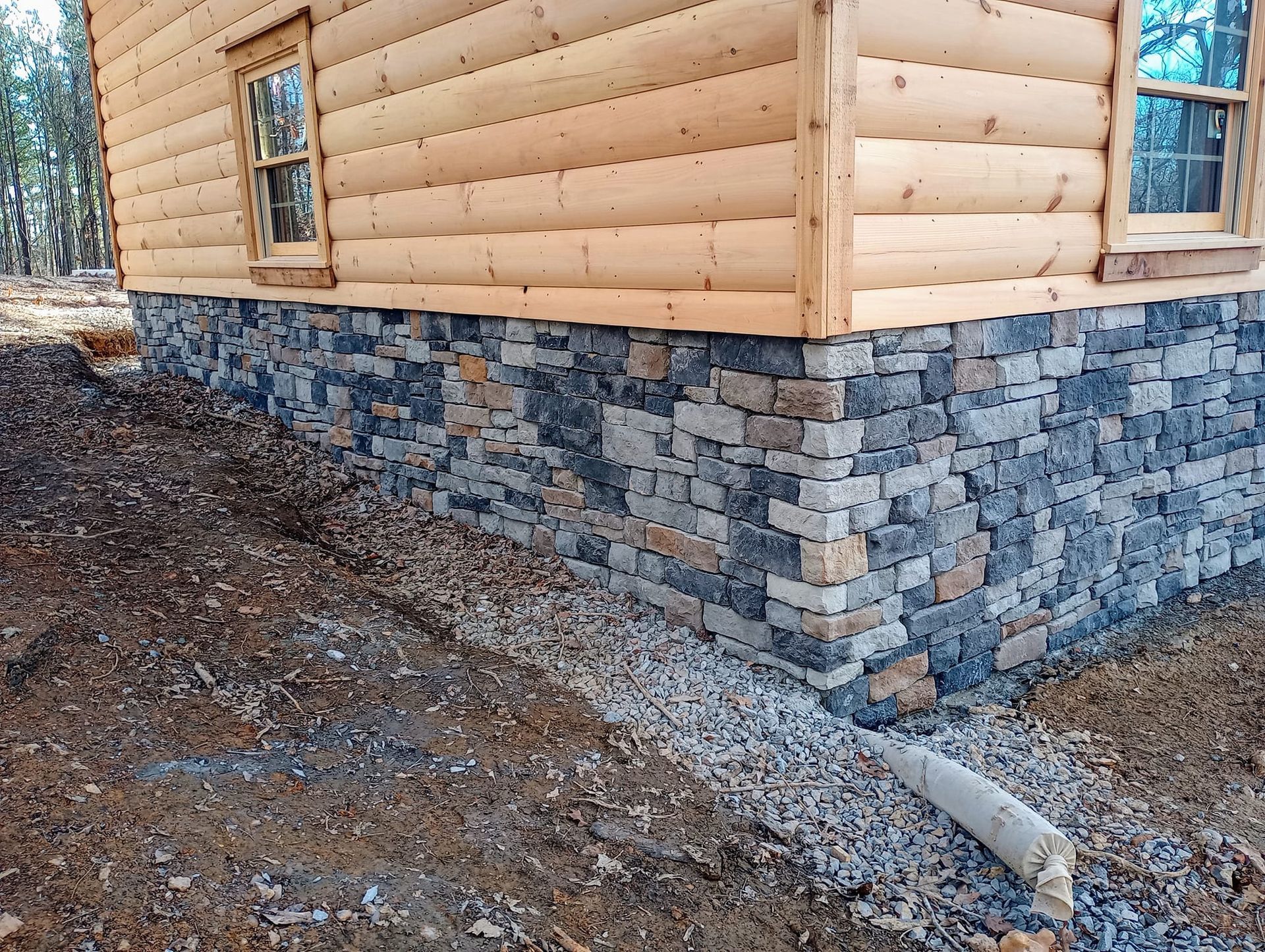 A log cabin with a stone foundation is sitting on top of a dirt hill.