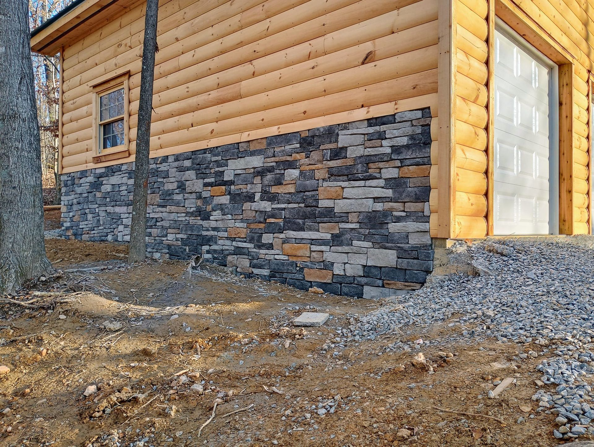 A log cabin with a stone wall and a garage door.