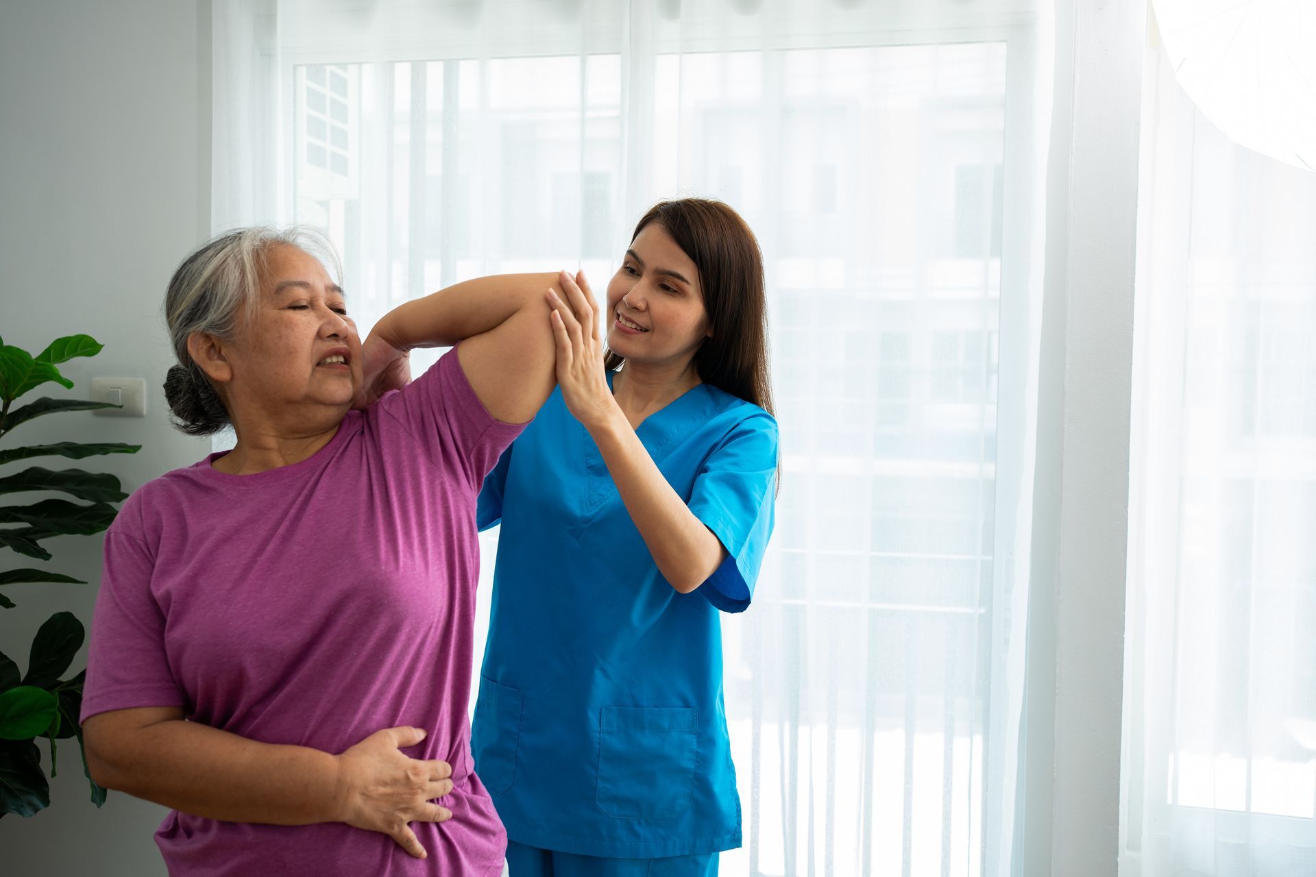A nurse is helping an elderly woman stretch her arms.