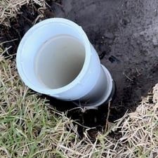 A white pipe is sitting in a hole in the ground.